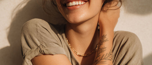 Smiling woman with a large botanical-style semi-permanent herbal temporary tattoo on her forearm, plant-based ink design, natural daylight.