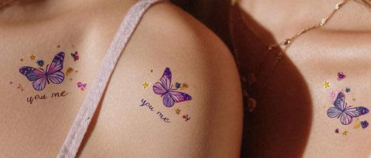 Close-up of two women’s shoulders with matching purple butterfly temporary tattoos, reading “you me”, colorful design, aesthetic body art.