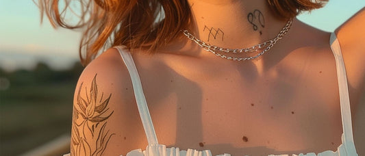 Stylish young woman outdoors with a large botanical-style temporary tattoo on her upper arm and minimalist tattoos on her neck, natural sunlight.